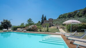 A swimming pool with wooden deck and lounge chairs, surrounded by greenery and a house in the background. - Casolare Torre With Pool And Ac (Poggibonsi)