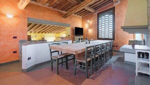 A spacious kitchen with a large island, wooden ceiling beams, and a view through a window with a lattice design. - Casolare Torre With Pool And Ac (Poggibonsi)