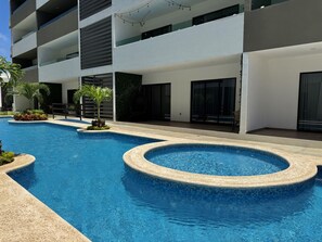 Una piscina con borde de azulejos, rodeada por un edificio con balcones y techo plano.