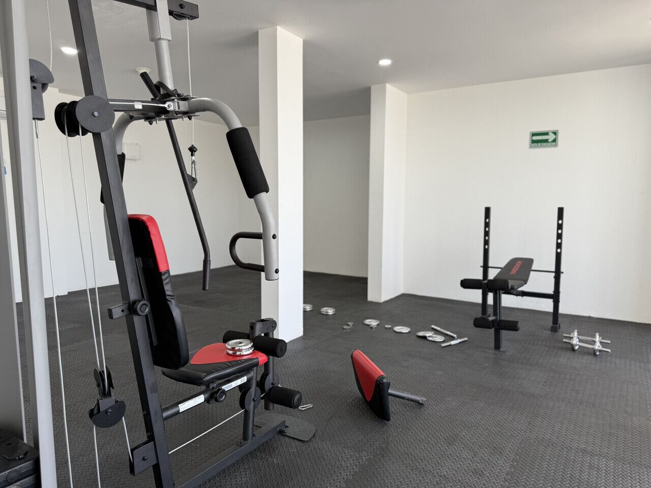 Une salle de sport équipée de matériel d’exercice, d’un banc et d’une enseigne fixée au mur.
