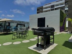 Un patio exterior con césped artificial, una parrilla y mobiliario para exteriores.