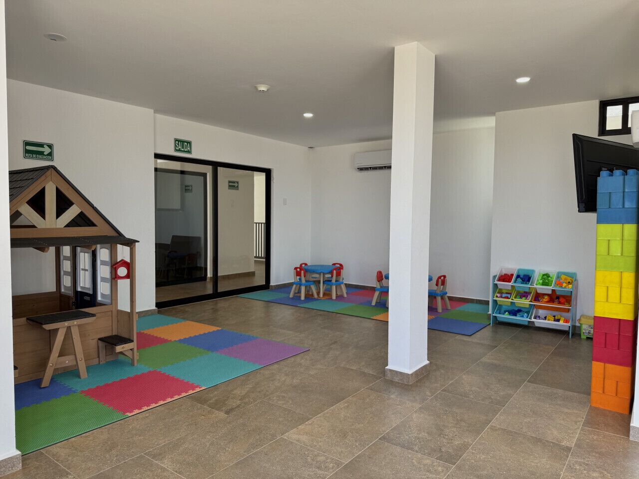 Zona de juegos infantiles con una casita de madera, alfombras de colores y un mueble para guardar juguetes.