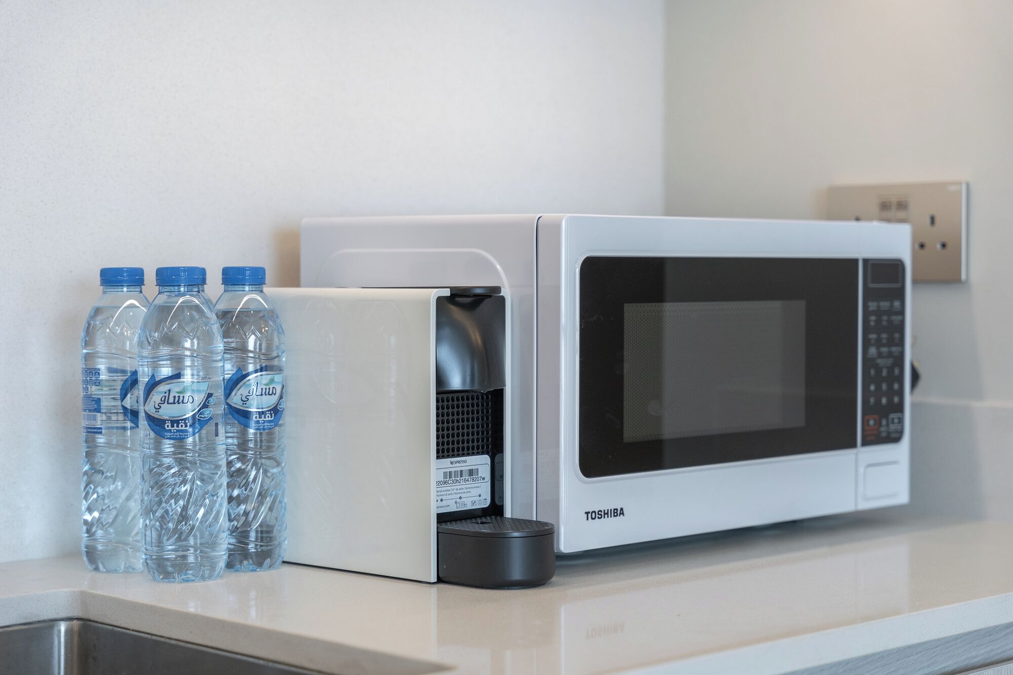 Une cuisine équipée d’un four à micro-ondes et de bouteilles d’eau posées sur le comptoir.