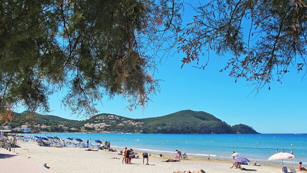 A beach with people sunbathing and swimming, a clear blue sky, and hills in the background. - Les Hauts du Port by Interhome (Saint Cyr sur mer Les Lecques)