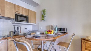 A compact kitchen with wooden cabinets, a microwave, a kettle, and a fruit bowl on the counter. - Les Hauts du Port by Interhome (Saint Cyr sur mer Les Lecques)