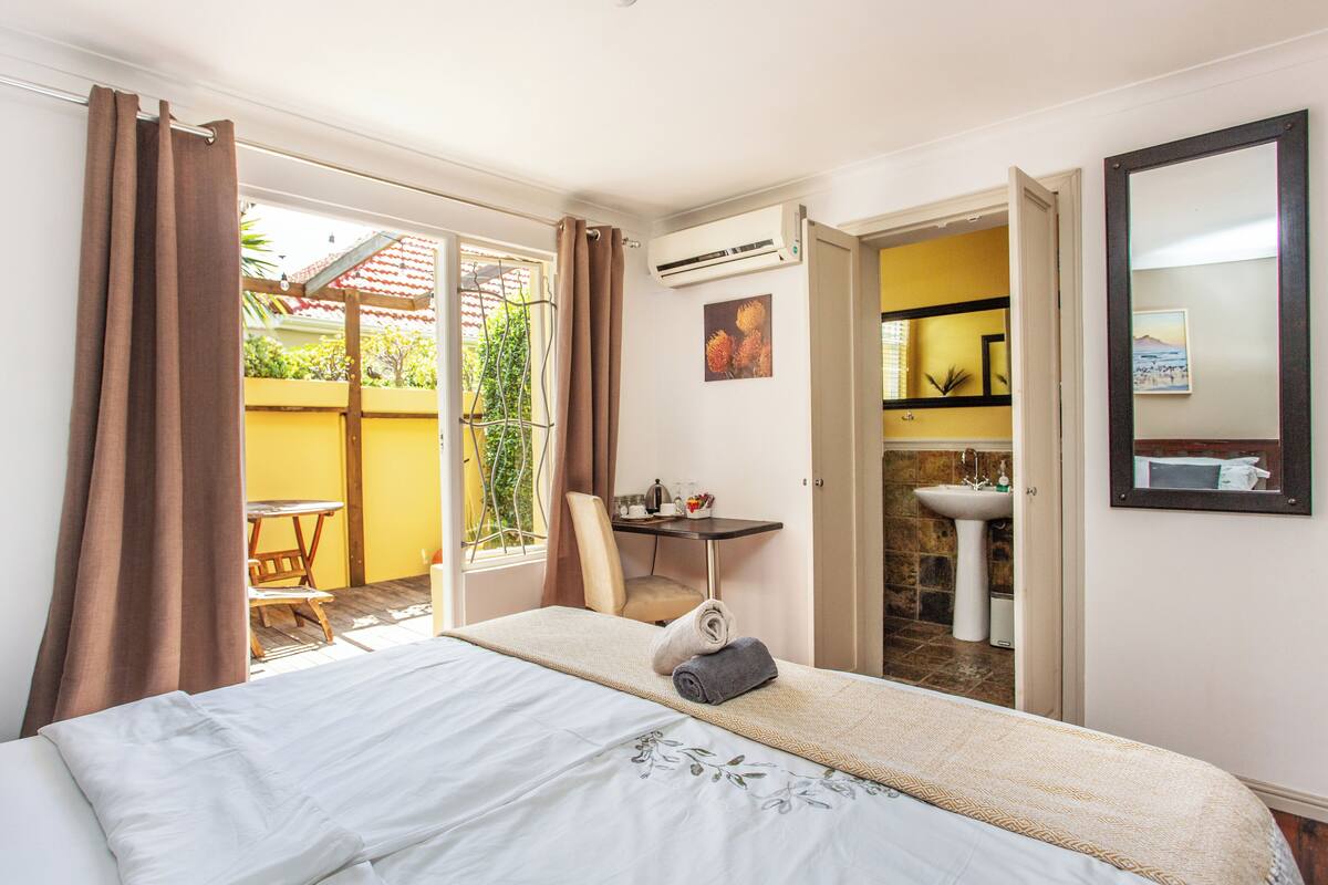 A hotel room with a bed, a desk, a chair, a bathroom with a sink, and a large mirror.