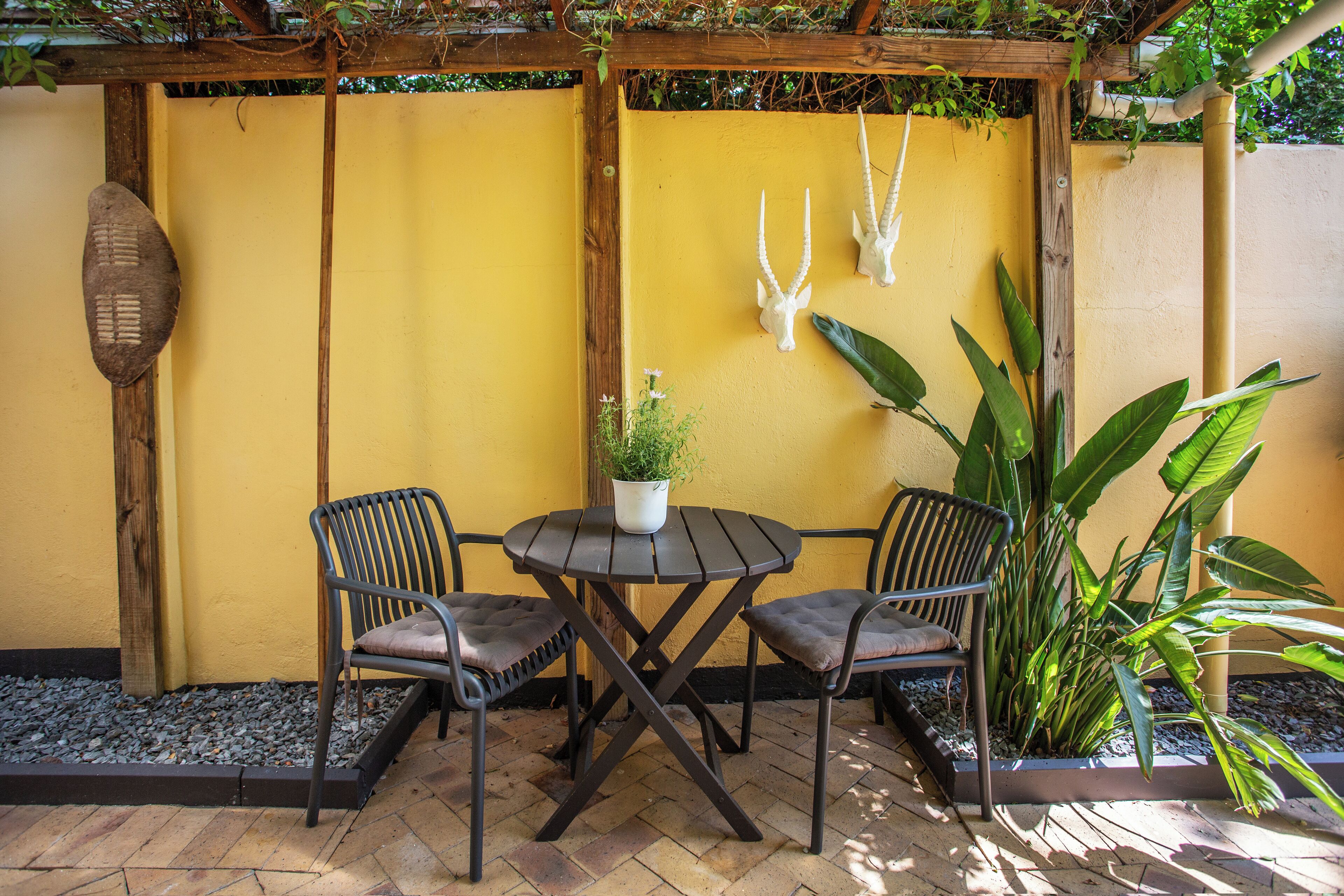 Pátio com duas cadeiras, uma mesa e objetos decorativos em frente a uma parede amarela.