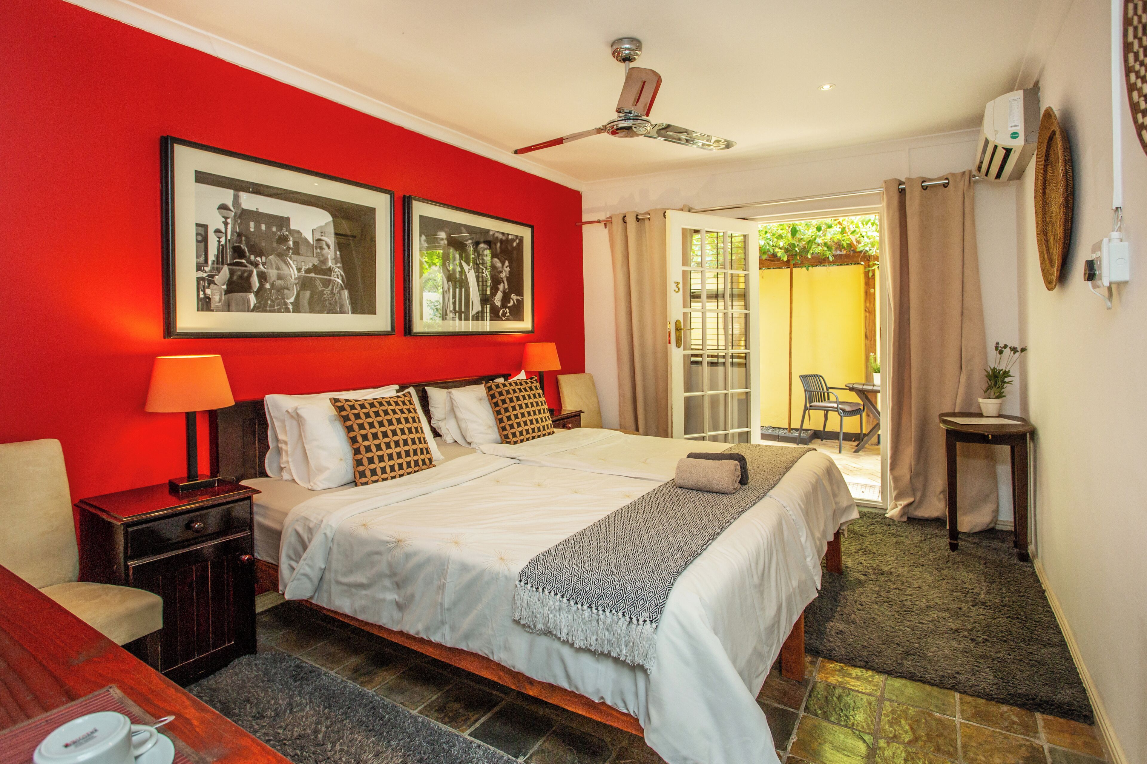 A hotel room with a large bed, two bedside tables, a ceiling fan, and a view of the outside.