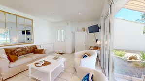 A modern living room with a white sofa, a white armchair, and a coffee table. There is a large window with a view of the outdoors.