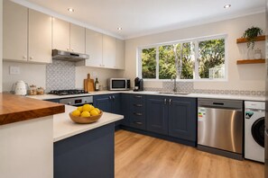 Une cuisine moderne dotée d’un îlot central, d’appareils électroménagers intégrés et d’une grande fenêtre offrant une vue sur la verdure.
