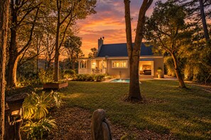 A two-story house with a swimming pool, surrounded by trees and a well-maintained lawn.