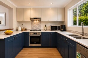 A modern kitchen with dark blue cabinets, a stainless steel range, a microwave, and a built-in oven.