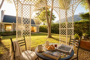 A gazebo with a table set for breakfast, including croissants, coffee, and a newspaper.