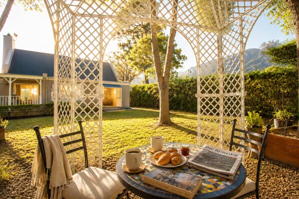 A gazebo with a table set for breakfast, including croissants, coffee, and a newspaper.