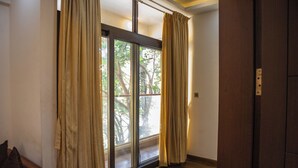 A room with a large sliding glass door leading to a balcony, a wooden floor, and a brown door. - Mystic Apartotel Hebbal (Bengaluru)