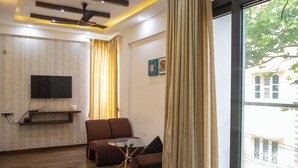 A living room with a flat-screen TV mounted on the wall, a sofa, a small round table, and a window with curtains. - Mystic Apartotel Hebbal (Bengaluru)