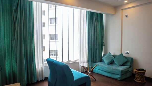A modern living room with a teal sofa, a glass coffee table, and a wicker side table. - Mystic Apartotel Hebbal (Bengaluru)