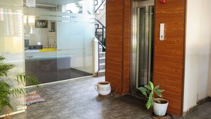 A reception area with a glass wall, wooden paneling, a reception desk, a potted plant, and an elevator. - Mystic Apartotel Hebbal (Bengaluru)