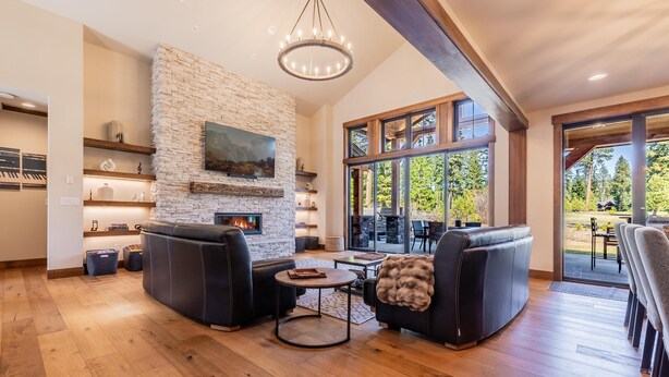 A spacious living room with a stone fireplace, leather sofas, and a large window offering a view of the outdoors.