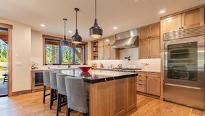 A modern kitchen with wooden cabinets, a stainless steel refrigerator, and a central island with bar stools.