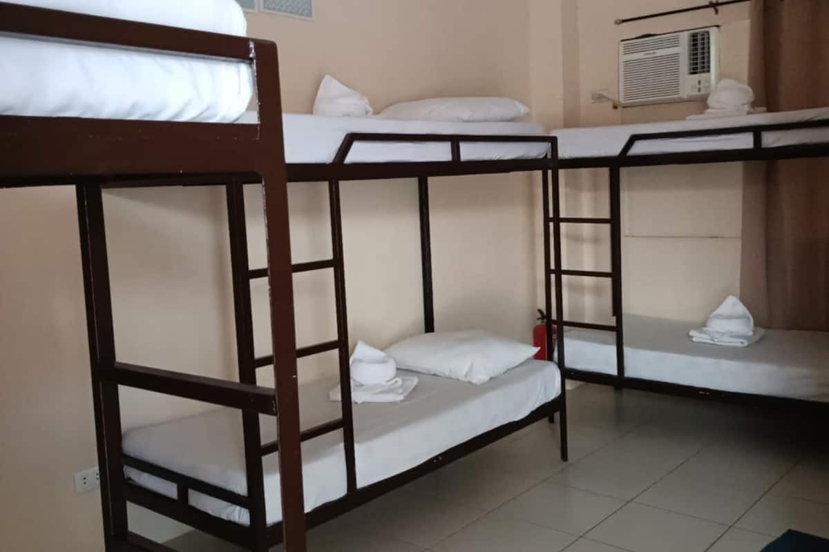 A dormitory room with bunk beds, a wall-mounted air conditioner, and a 'be kind' poster.