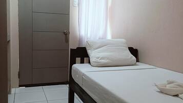Ein kleines, sauberes Zimmer mit einem Einzelbett, einer Tür und einem mit Vorhängen versehenen Fenster.