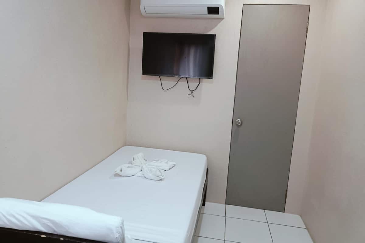 A small, clean room with a bed, a TV mounted on the wall, and a door.
