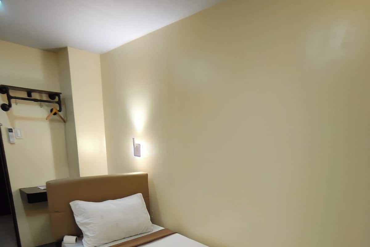 A single bed with a wooden headboard, a white mattress, and a neatly folded white towel.