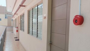Un pasillo con piso de baldosas, una puerta con la etiqueta “204” y un detector de incendios en la pared.