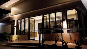 Una casa moderna con una amplia puerta de cristal, un balcón y plantas en macetas al frente.