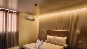 Una habitación de hotel moderna con una cama grande, una mesita de noche, aire acondicionado instalado en la pared y una ventana con cortinas.