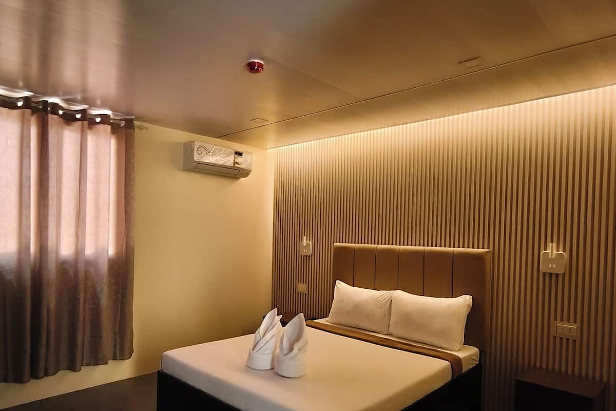 A modern hotel room with a large bed, a bedside table, a wall-mounted air conditioner, and a window with curtains.