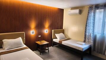 Habitación de hotel con dos camas, una mesita pequeña, aire acondicionado instalado en la pared y una ventana con cortinas.