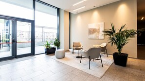 A modern lobby with a glass door entrance, a seating area with chairs, a large potted plant, and a painting on the wall. - East Uptown P Pasolini 74 Cascina Merlata (Milan)