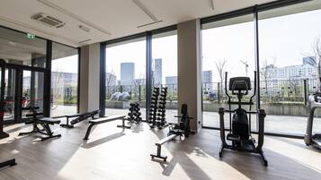 Une salle de sport moderne dotée de grandes fenêtres, de divers appareils d’exercice et offrant une vue sur le paysage urbain.