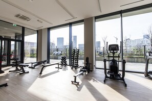A modern gym with large windows, various exercise equipment, and a view of the cityscape. - East Uptown P Pasolini 74 Cascina Merlata (Milan)
