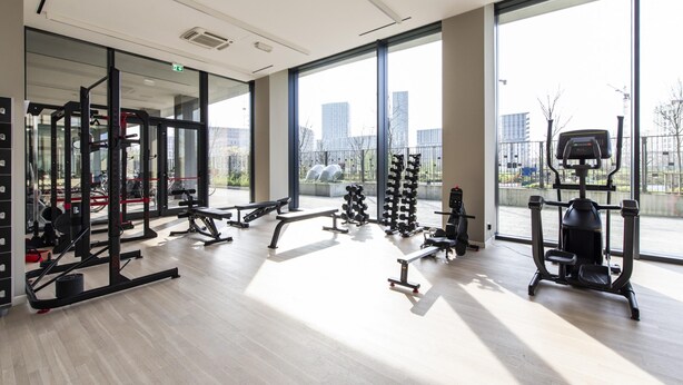 A modern gym with various exercise equipment, large windows, and a view of the cityscape. - East Uptown P Pasolini 74 Cascina Merlata (Milan)