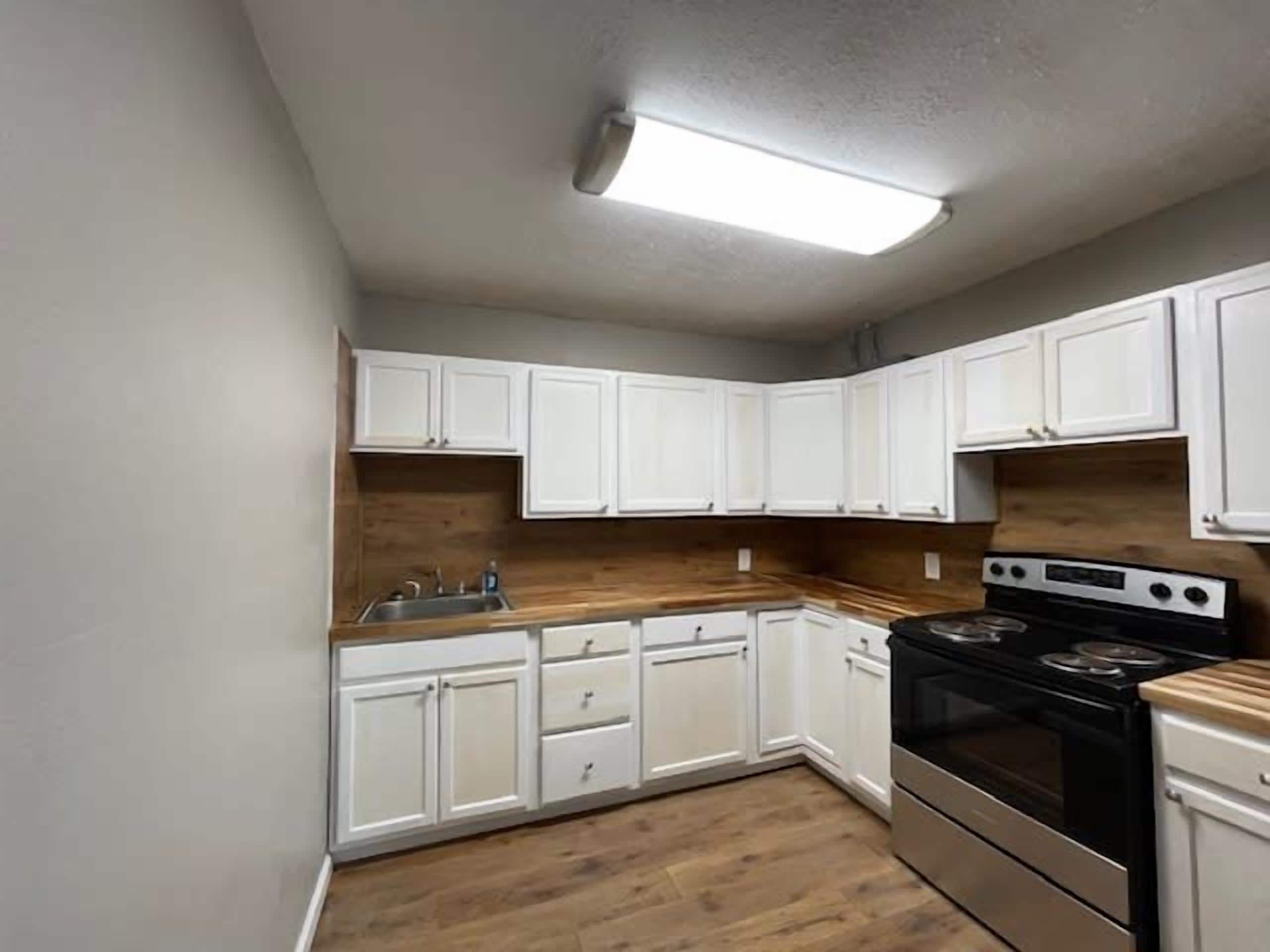 A kitchen with white cabinets, a wooden countertop, a stainless steel stove, and a built-in oven.