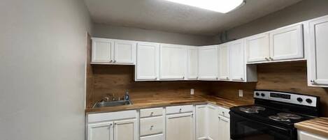 A kitchen with white cabinets, a wooden countertop, a stainless steel stove, and a built-in oven.