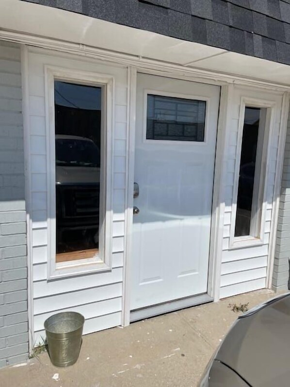 A white door with a window, a metal bucket on the ground, and a vehicle parked nearby. - Cozy 1-Bed, 1-Bath with Full Kitchen Near Fort Sill (Lawton)