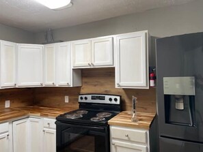 A kitchen with white cabinets, a black stove, and a stainless steel refrigerator. - Cozy 1-Bed, 1-Bath with Full Kitchen Near Fort Sill (Lawton)