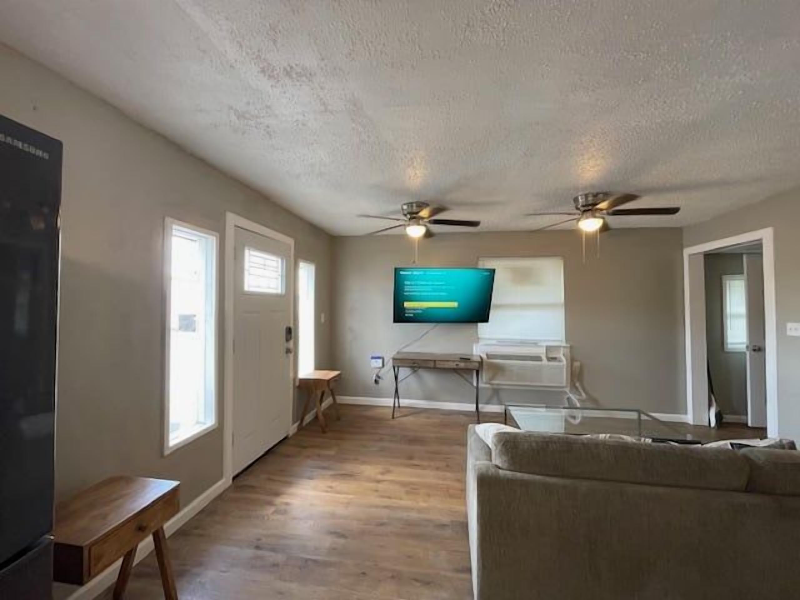 A living room with a flat-screen TV mounted on the wall, a ceiling fan, and a wooden bench.