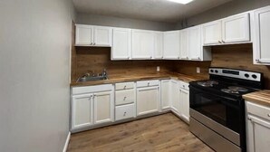 Une cuisine compacte avec des meubles blancs, un plan de travail en bois, une cuisinière en acier inoxydable et un four encastré.