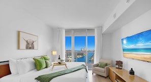 A modern hotel room with a large bed, a city view, a beach view, and a framed artwork. - Infinite View, Amazing Apt, Spectacular Amenities (Hallandale Beach)