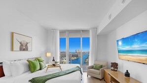 A modern hotel room with a large bed, a city view, a beach view, and a framed artwork. - Spectacular Apt, Infinity View, Amazing Amenities (Hallandale Beach)