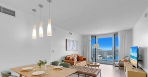 A modern living room with a dining area, large windows with a city view, and a flat-screen TV. - Spectacular Apt, Infinity View, Amazing Amenities (Hallandale Beach)