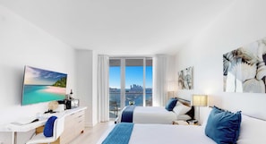 A modern hotel room with a large bed, a desk, a flat-screen TV, and a balcony with a city view.