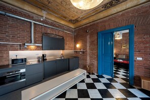 A modern kitchen with a black and white checkered floor, a blue door, and a brick wall.