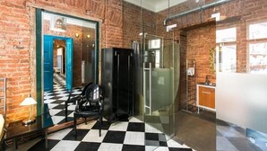 A modern hotel room with a brick wall, a checkered floor, a glass shower enclosure, and a black refrigerator.