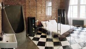A modern bedroom with a checkered floor, a large bed, a glass shower enclosure, and a brick wall.